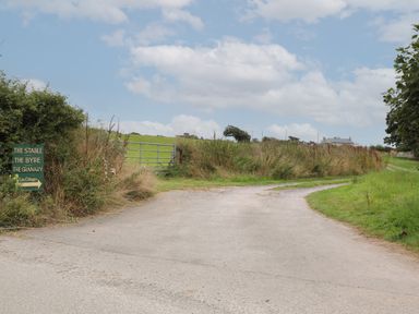 A country road with a fork and a green directional sign for cottages near a gate and grassy fields at The Granary Rhoscolyn
