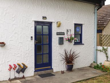 The front entrance of a white textured wall building with a blue door and window at The Granary in Rhoscolyn