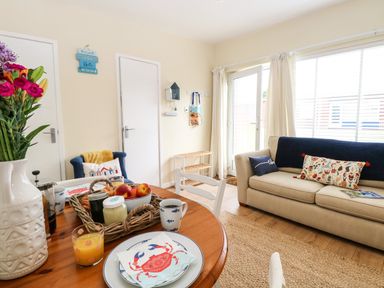 A living room with a beige sofa and a wooden dining table set with breakfast items at The Cranny in Mundesley