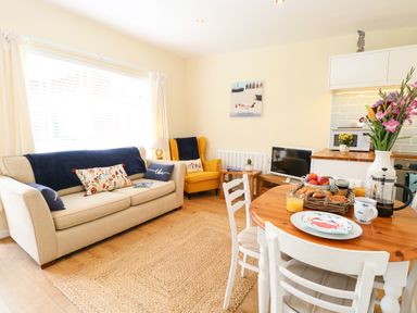 A living room with a beige sofa and yellow armchair and a dining table set with breakfast at The Cranny in Mundesley
