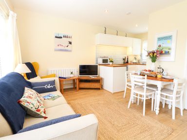 A living room with a sofa and armchair next to a small TV and a dining table with chairs near a kitchen at The Cranny in Mundesley
