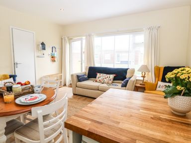 A living room with a beige sofa a yellow armchair a wooden dining table and white chairs at The Cranny in Mundesley