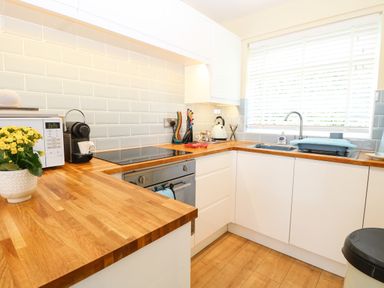 A kitchen with wooden countertops white cabinets a microwave coffee maker and a window with blinds at The Cranny in Mundesley