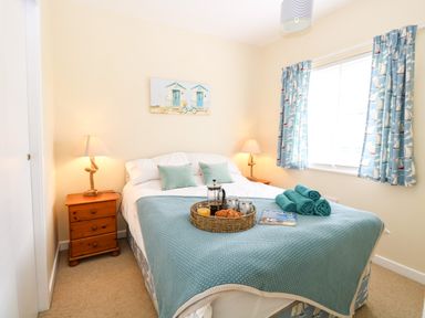A bedroom with a double bed bedside tables lamps and a window with patterned blue curtains at The Cranny in Mundesley