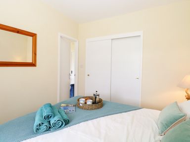 A bedroom with a bed, rolled towels, a tray with cups, a mirror, and a closet with sliding doors at The Cranny in Mundesley