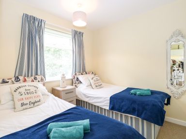 A bedroom with two single beds blue blankets and rolled towels a window with striped curtains and a decorative wall mirror at The Cranny in Mundesley