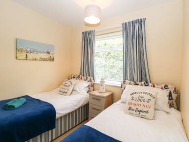 A bedroom with two single beds a nightstand and a window with blue curtains at The Cranny in Mundesley