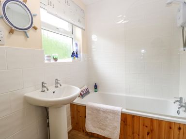 A bathroom with a pedestal sink a bathtub with wooden paneling and a window above at The Cranny in Mundesley