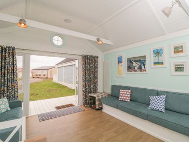 A living room with blue sofas and patterned cushions with framed pictures on the wall at Shore Thing 280 in Wilsthorpe