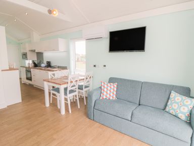 A kitchen and living area with a dining table and chairs a sofa with cushions and a wall-mounted television at Shore Thing 280 in Wilsthorpe