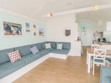 An open living room and kitchen area with a blue sectional sofa and dining table with chairs at Shore Thing 280 in Wilsthorpe