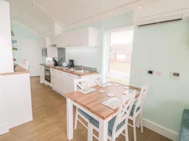 A kitchen with wooden countertops a dining table with four chairs and placemats and a window with blinds at Shore Thing 280 in Wilsthorpe