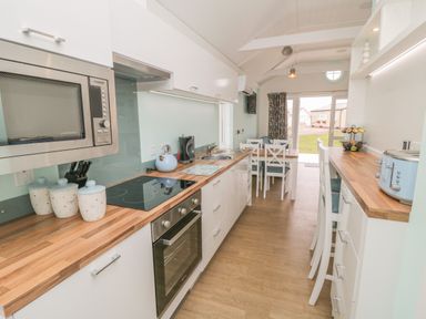 A kitchen with wooden countertops white cabinets a microwave stove kettle toaster and a dining table at Shore Thing 280 in Wilsthorpe
