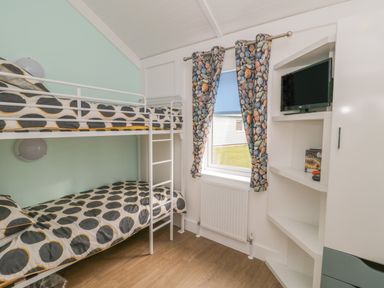 A bedroom with bunk beds and a TV mounted in shelves near a window with stone patterned curtains at Shore Thing 280 in Wilsthorpe