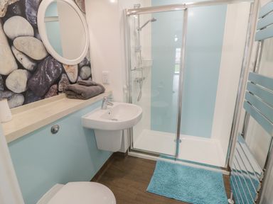 A bathroom with a sink a shower enclosure a blue rug wall heater and a round mirror above a countertop at Shore Thing 280 in Wilsthorpe