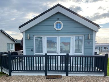 A small blue wooden house with white trim and a black railing fence at Shore Thing 280 in Wilsthorpe