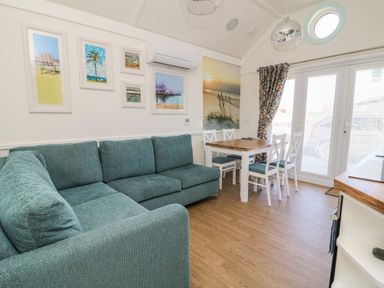 A living room with teal sofa white dining table and chairs framed beach pictures at Shore Thing 279 in Wilsthorpe