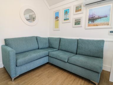 A corner sofa with blue upholstery against white walls with framed pictures and a round mirror at Shore Thing 279 in Wilsthorpe