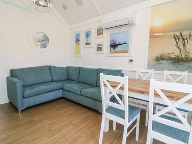A corner sofa and dining table with chairs in a room with framed pictures and an air conditioner at Shore Thing 279 in Wilsthorpe