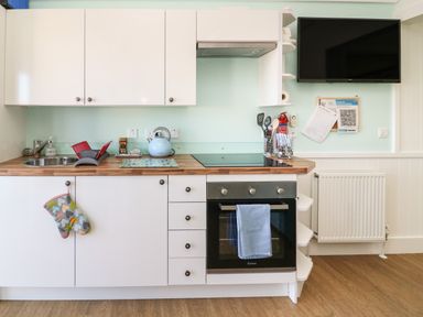 A kitchen with white cabinets wooden countertop oven and sink with a blue kettle a television mounted on the wall at Shore Thing 279 in Wilsthorpe