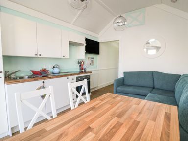 A kitchen and dining area with white cabinets wooden countertop a dining table with white chairs and a teal corner sofa at Shore Thing 279 in Wilsthorpe