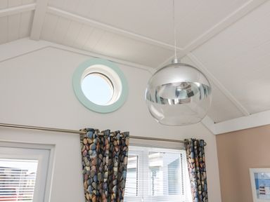 A room with a round window a silver hanging lamp and curtains with a pebble pattern at Shore Thing 279 in Wilsthorpe
