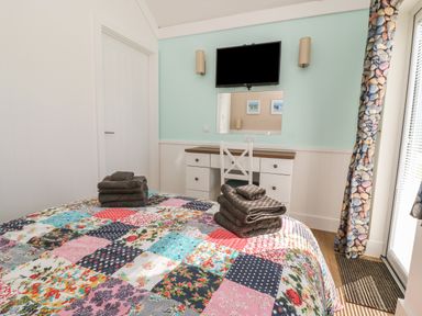A bedroom with a colorful patchwork quilt on the bed a white desk with drawers a wall-mounted tv and a patterned curtain at Shore Thing 279 in Wilsthorpe