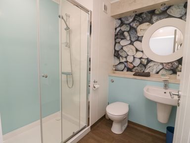 A bathroom with a glass shower enclosure a toilet a wall-mounted sink and a round mirror above a countertop with a stone patterned backsplash at Shore Thing 279 in Wilsthorpe