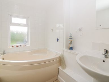 A bathroom with a corner bathtub a window with seashells on the sill a sink with a faucet a mirror and a lighthouse decoration