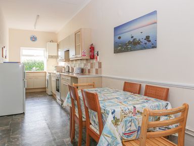 A kitchen with a dining table and chairs a stove a washing machine and a refrigerator at Gull Cottage in Tintagel