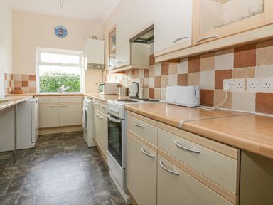 A kitchen with beige cabinets brown tiled backsplash and appliances at Gull Cottage in Tintagel
