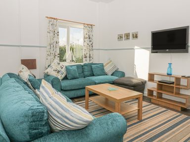 A living room with two teal sofas a wooden coffee table a wall-mounted television and a shelving unit at Gull Cottage in Tintagel