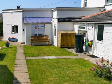 A backyard with a stone pathway wooden bench rainwater barrel and garden hose at Gull Cottage in Tintagel