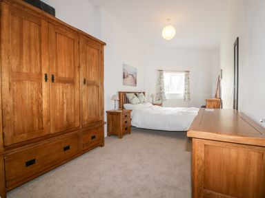 A bedroom with wooden furniture including wardrobe bed side tables and a dresser at Gull Cottage in Tintagel