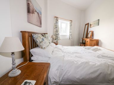 A bedroom with a wooden bed frame bedside table with lamp and a wooden dresser with mirror at Gull Cottage in Tintagel