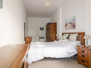 A bedroom with a double bed wooden furniture and white bedding at Gull Cottage in Tintagel