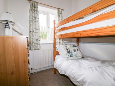 A bedroom with a wooden bunk bed a wooden chest of drawers and a window with curtains at Gull Cottage in Tintagel