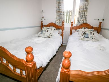 A bedroom with two wooden single beds with white bedding and patterned pillows at Gull Cottage in Tintagel