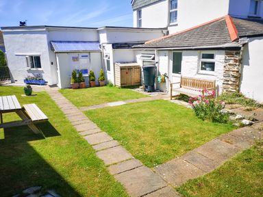 A backyard garden with a stone pathway wooden bench picnic table and potted plants at Gull Cottage in Tintagel