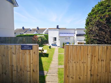 A garden path leading to a white cottage with a wooden fence and a picnic table at Gull Cottage Tintagel