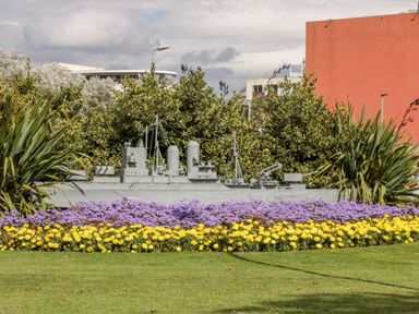 A garden with a model ship surrounded by purple and yellow flowers and green plants at Royal Victoria House in Scarborough
