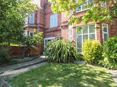 A garden with green grass plants and trees next to a red brick building at Royal Victoria House in Scarborough