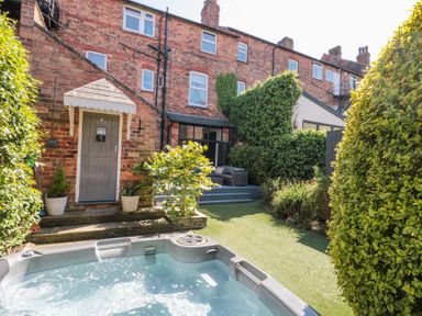 A backyard with a hot tub and patio furniture next to a brick house at Royal Victoria House in Scarborough