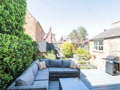 An outdoor patio with a sectional sofa and cushions a grill and plants at Royal Victoria House in Scarborough