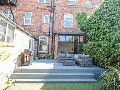 An outdoor patio with a sectional sofa a coffee table a barbecue grill and potted plants at Royal Victoria House in Scarborough