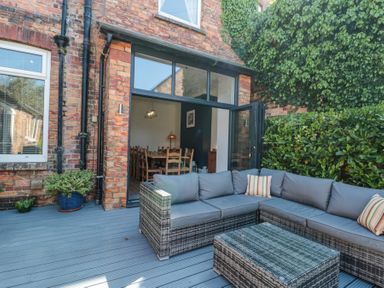 An outdoor patio area with wicker seating and cushions next to a brick building with an open door showing a dining area inside at Royal Victoria House in Scarborough