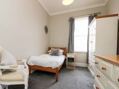 A bedroom with a bed, armchair, wardrobe, and dresser at Royal Victoria House in Scarborough