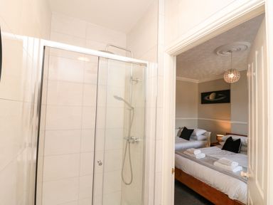 A bathroom with a shower and a view of a bedroom with two beds at Royal Victoria House in Scarborough