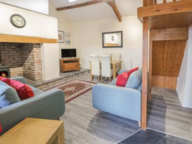 A living room with blue sofas red cushions a television on a wooden stand a dining table with four chairs and a fireplace at Crud yr Awel in Braichmelyn near Bethesda