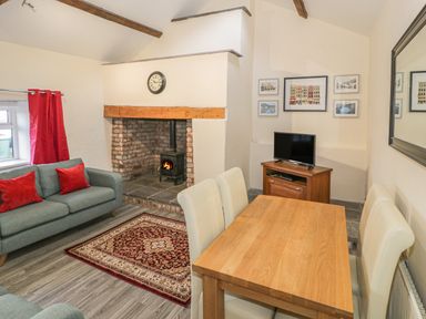 A living room with a wood burning stove a wooden dining table with four chairs a sofa with red cushions and wall art at Crud yr Awel in Braichmelyn near Bethesda